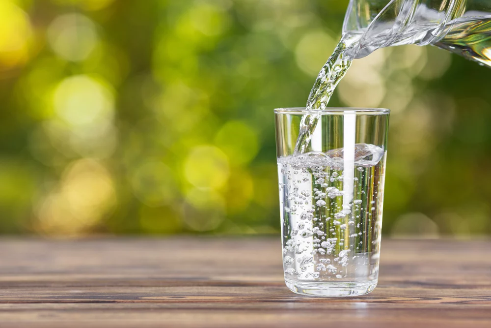 water,from,jug,pouring,into,glass,on,wooden,table,outdoors