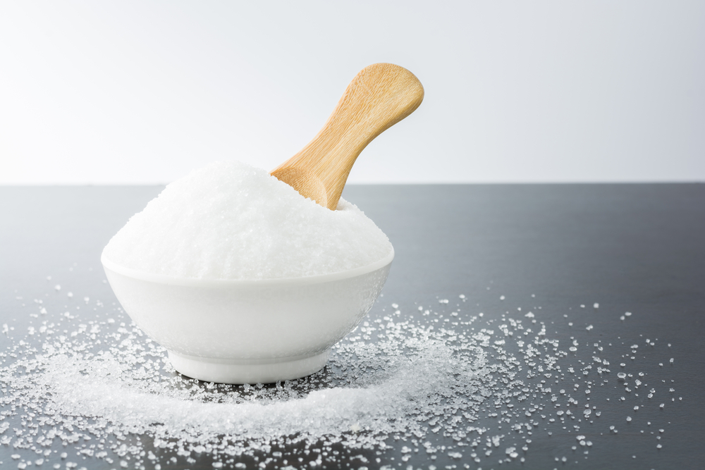 white,granulated,sugar,in,white,cup,with,wooden,spoon,on